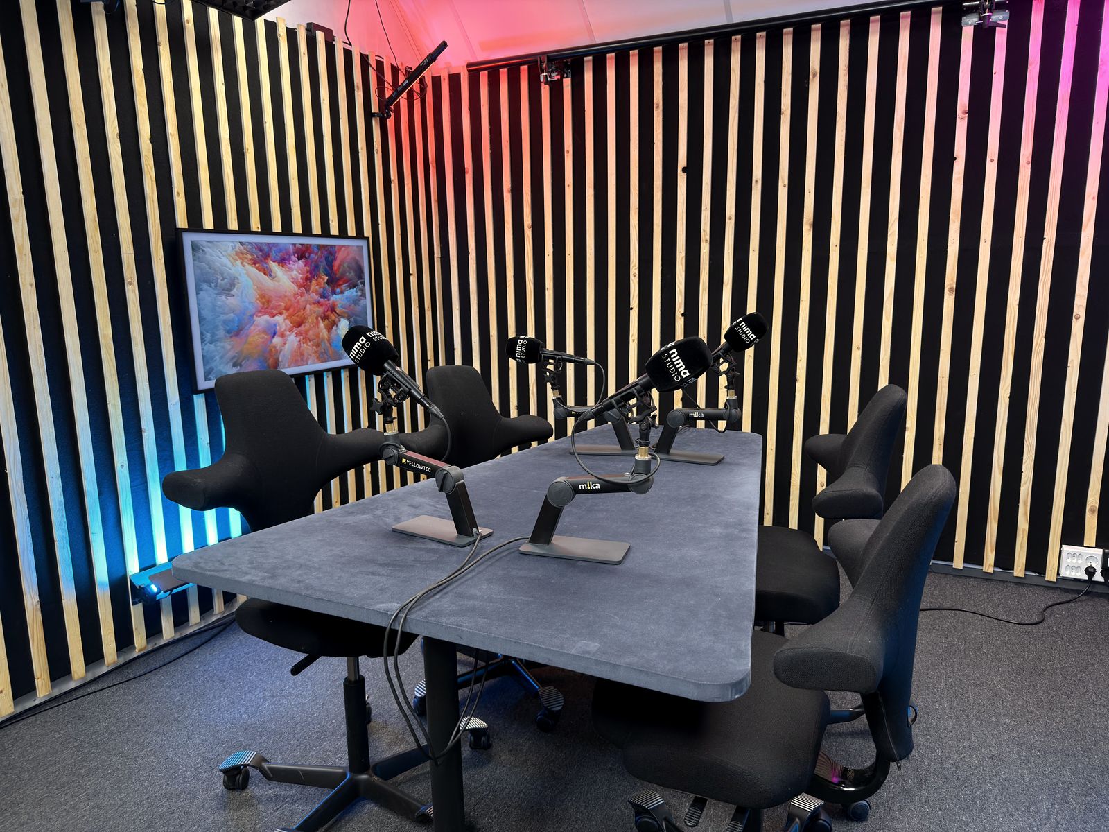 Podkaststudio A med bord, fire mikrofoner og fargelys